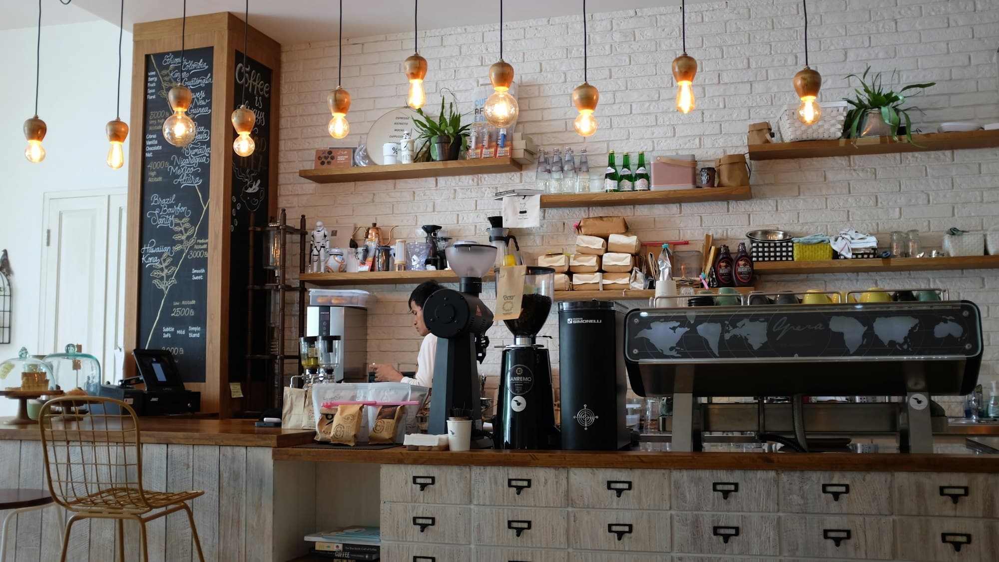The espresso bar under a row of copper pendant lights, chalkboard menu to the left.